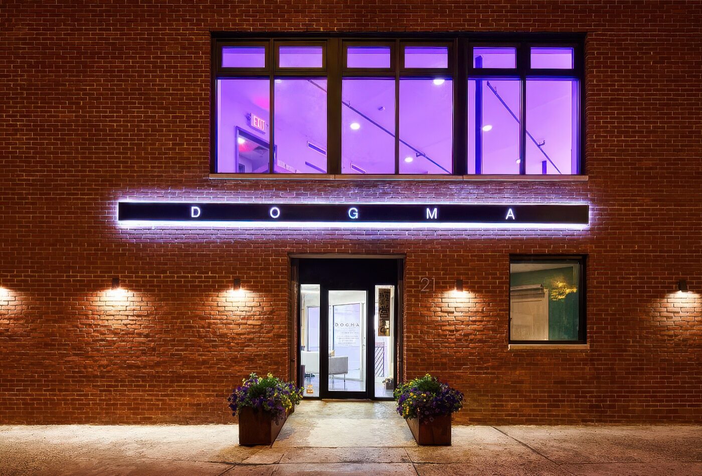 Night exterior of DOGMA with the illuminated neon DOGMA marquee on a red-brick facade