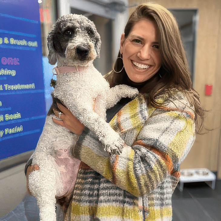 Woman in a colourful sweater holding a freshly groomed miniature poodle