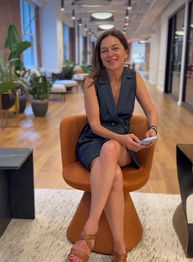 Woman in a navy sleeveless dress seated in an orange chair in a modern office lobby, smiling