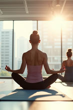 Woman meditating in lotus pose silhouetted against bright sunlit studio windows