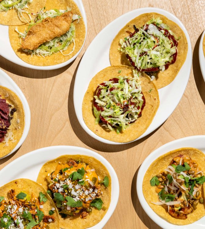 Overhead view of oval plates of assorted tacos on a wooden table.