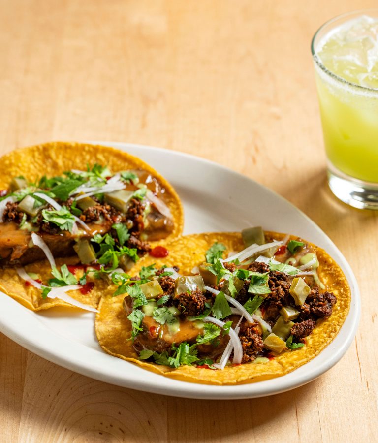 Two brisket suadero tacos on a white oval plate beside a specialty margarita at Empellón, 510 Madison.