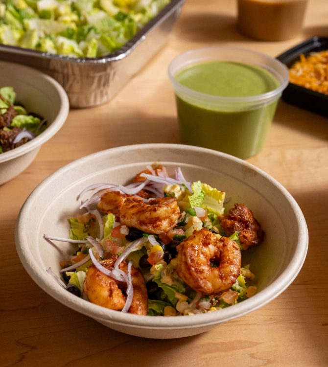A shrimp grain bowl beside Empellón catering trays.