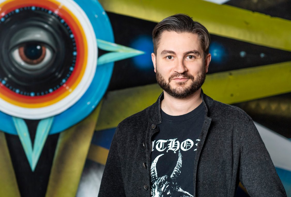 Chef Alex Stupak standing in front of a colorful street-art mural.