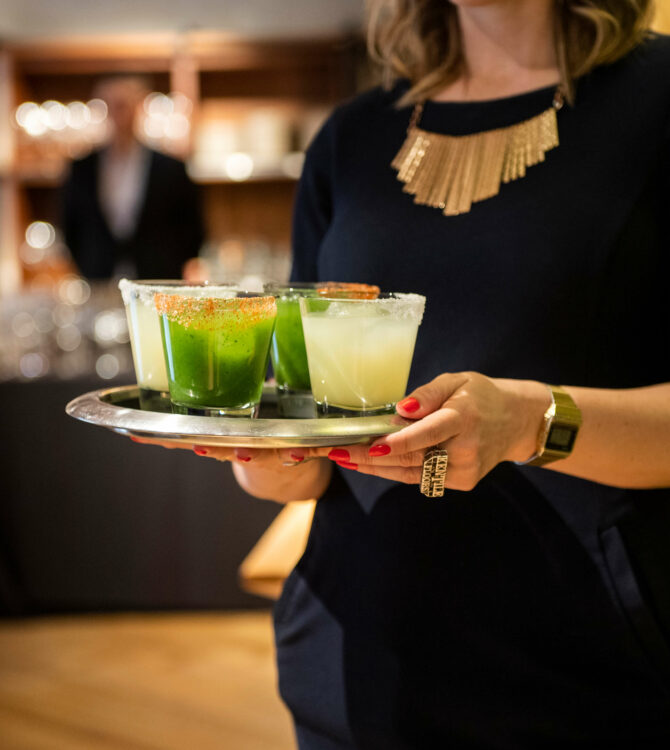 A server holds a silver tray of green and white margaritas at an Empellón event.