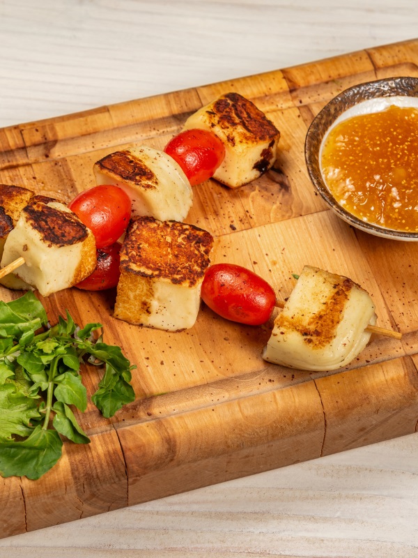 Halloumi and cherry tomato skewers on a wooden board with dipping sauce