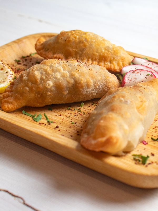 Lebanese fried meat pies on a wooden board with radish slices and lemon