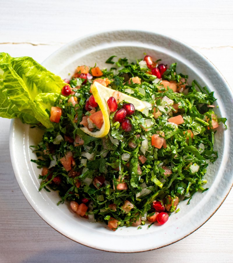 Tabbouleh with parsley, pomegranate seeds, tomato and a lemon slice