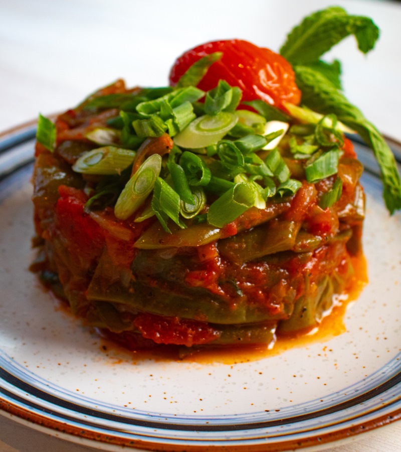 Lebanese stewed green beans and tomato garnished with scallions on a ceramic plate