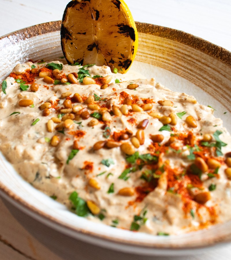 Baba ganoush dip with pine nuts, paprika, parsley and charred lemon in a ceramic bowl