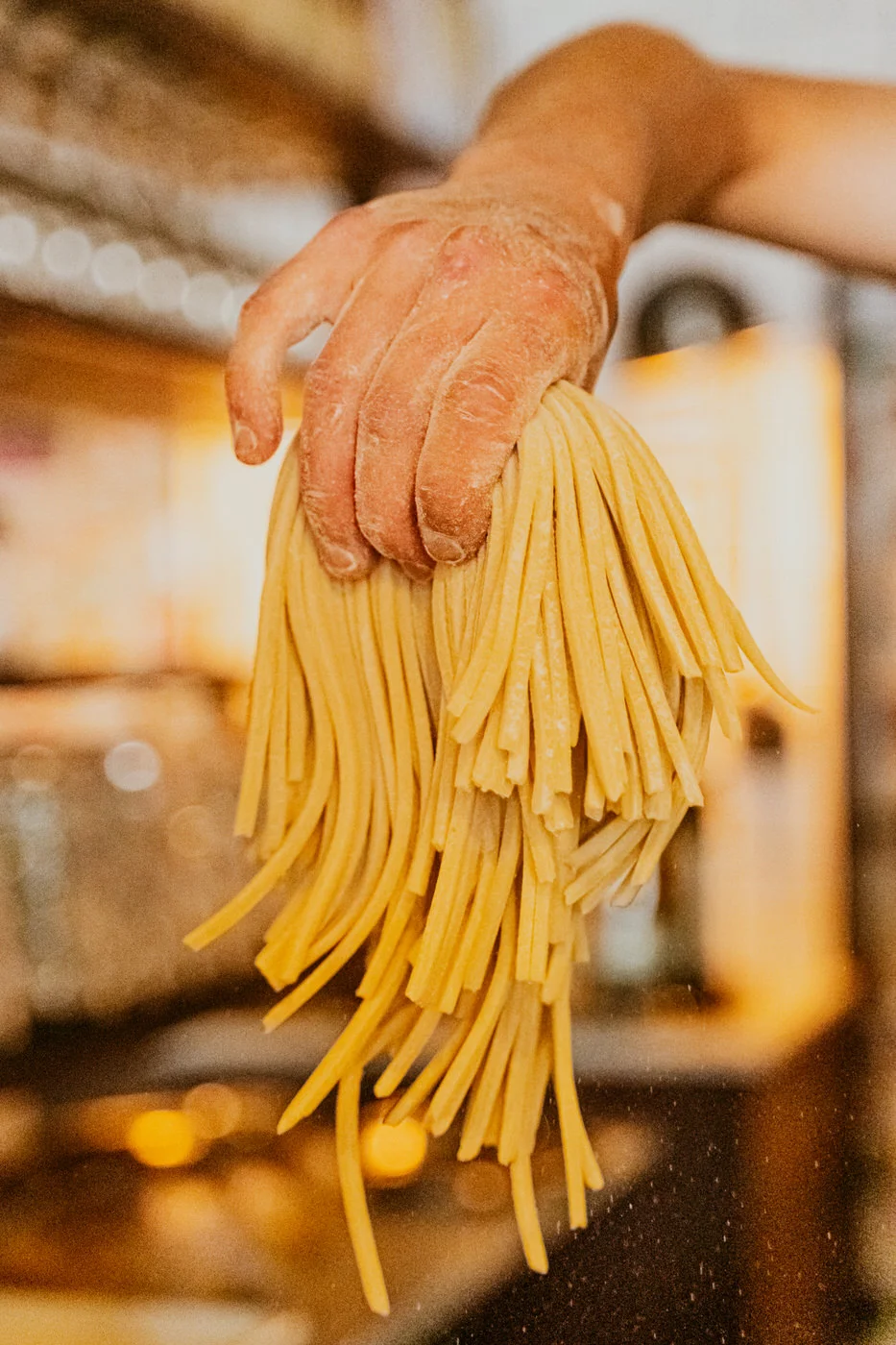 Flour-dusted hand holding a bundle of freshly made spaghetti strands