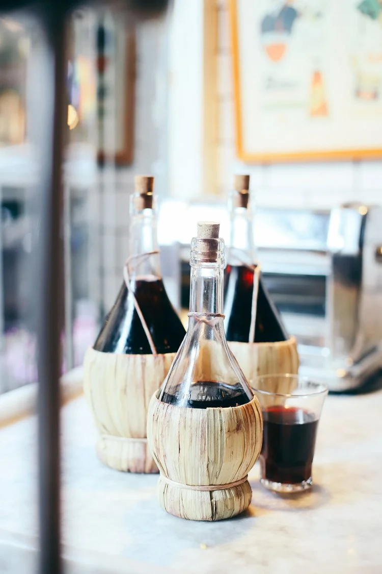 Three straw-wrapped fiasco wine bottles of red wine on a marble bar