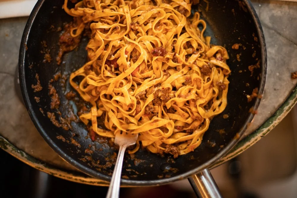 Tagliatelle bolognese being tossed in a well-seasoned pan on the stove