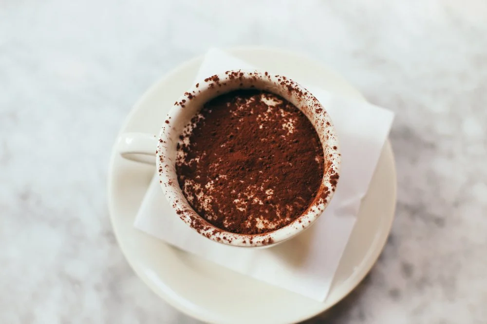 Cup of cocoa-dusted dessert on a saucer on a marble surface