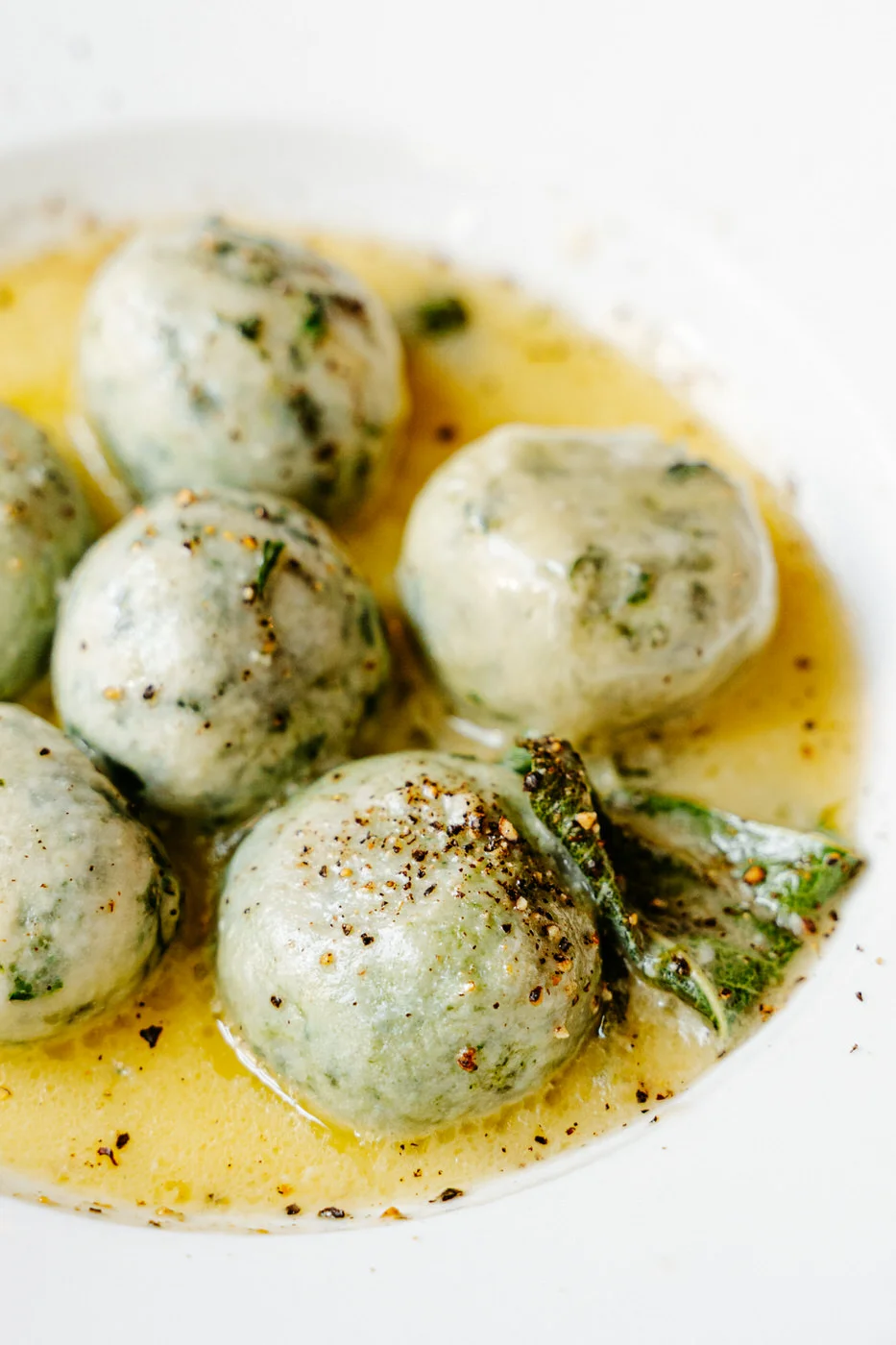 Herb gnudi, spinach and ricotta dumplings, in browned butter with sage on a white plate