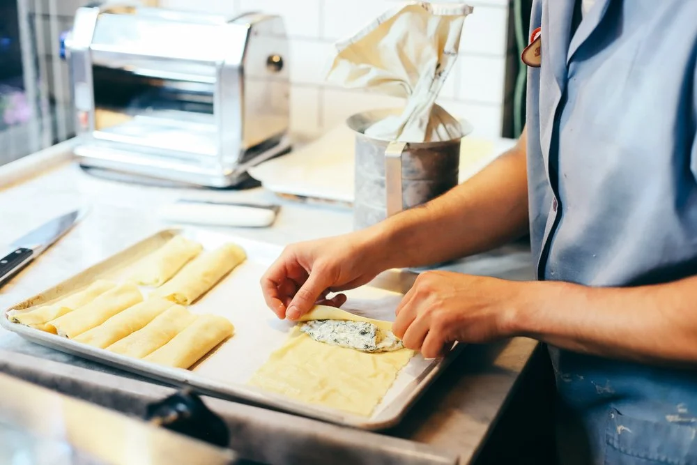 Chef's hands rolling and filling fresh cannelloni with a pasta machine behind