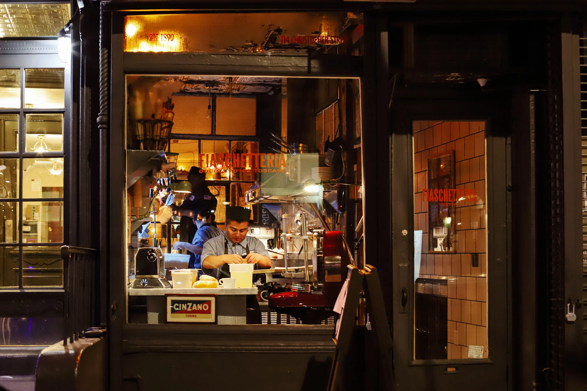 Night shot through the door of the West Village room, staff working at the bar, Cinzano sign visible