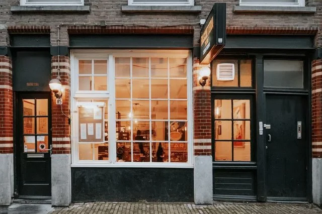 Brick shopfront in Amsterdam Centrum with a large lit window at dusk