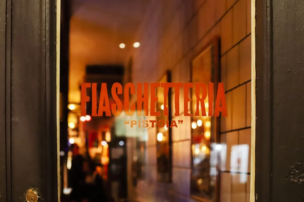 Fiaschetteria Pistoia name painted on the glass door with warm interior light behind
