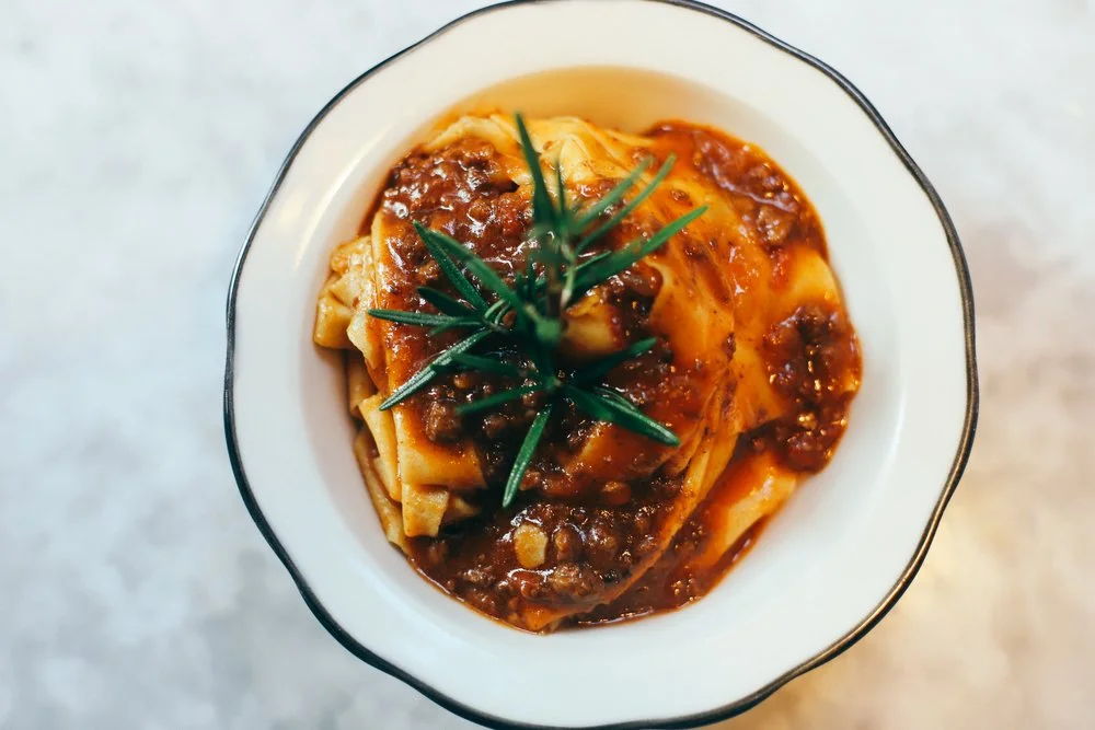 Pappardelle with meat ragù and rosemary garnish in a black-rimmed bowl