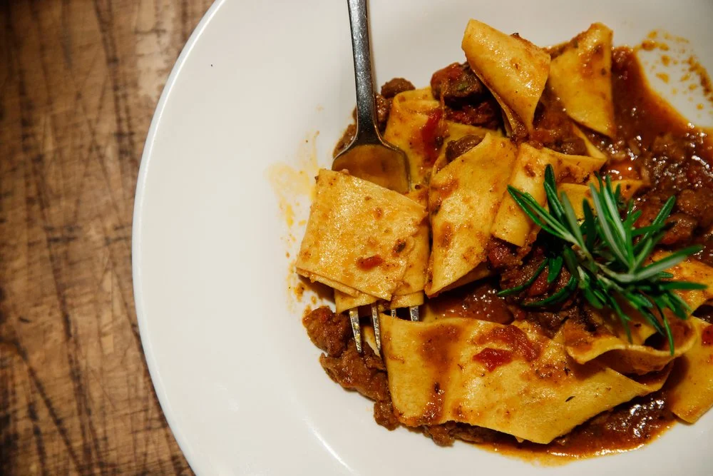 Pappardelle with braised meat ragù and a rosemary sprig on a white plate