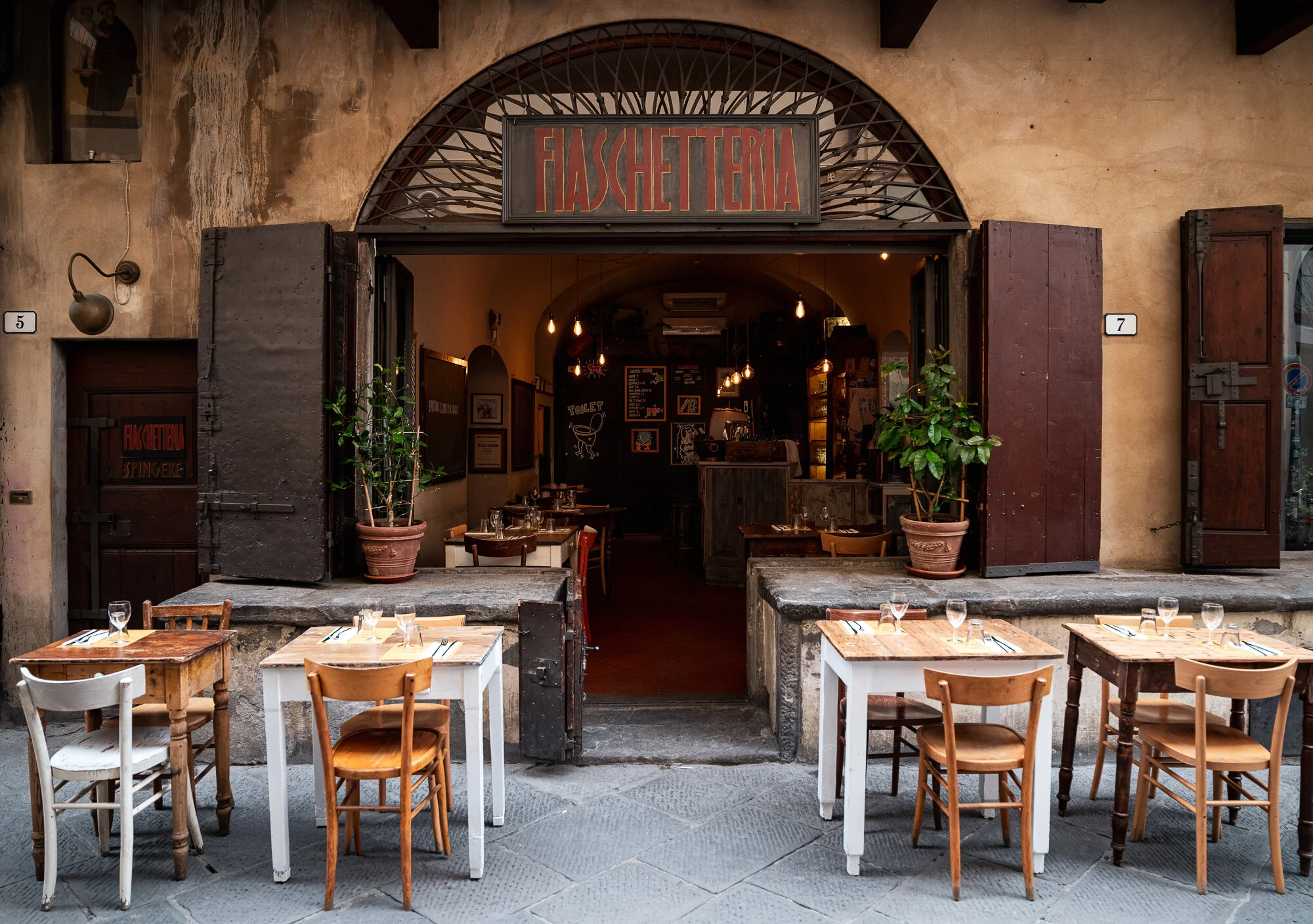 Pistoia storefront with an arched iron Fiaschetteria sign, wooden shutters and rustic tables on the cobbles