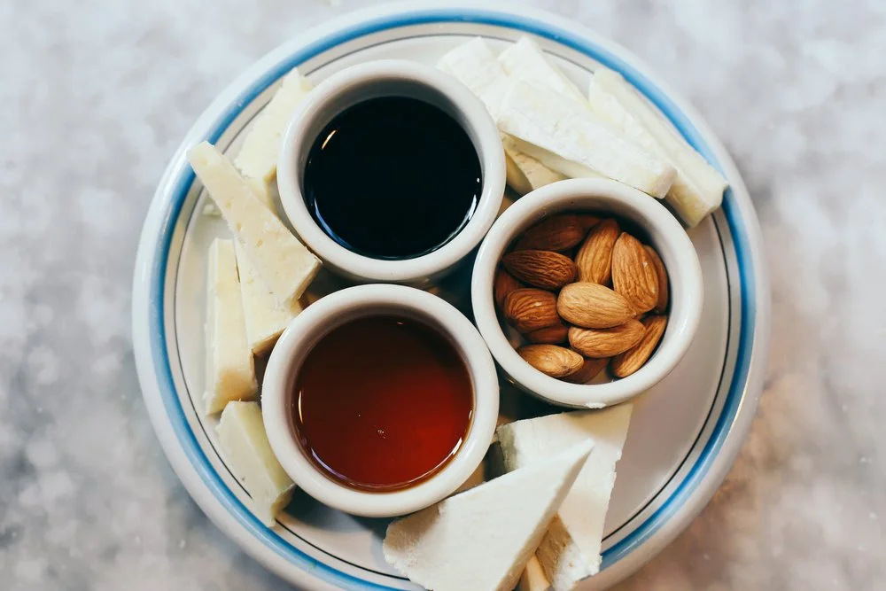 Cheese plate with white cheese slices, honey, balsamic and almonds in small bowls