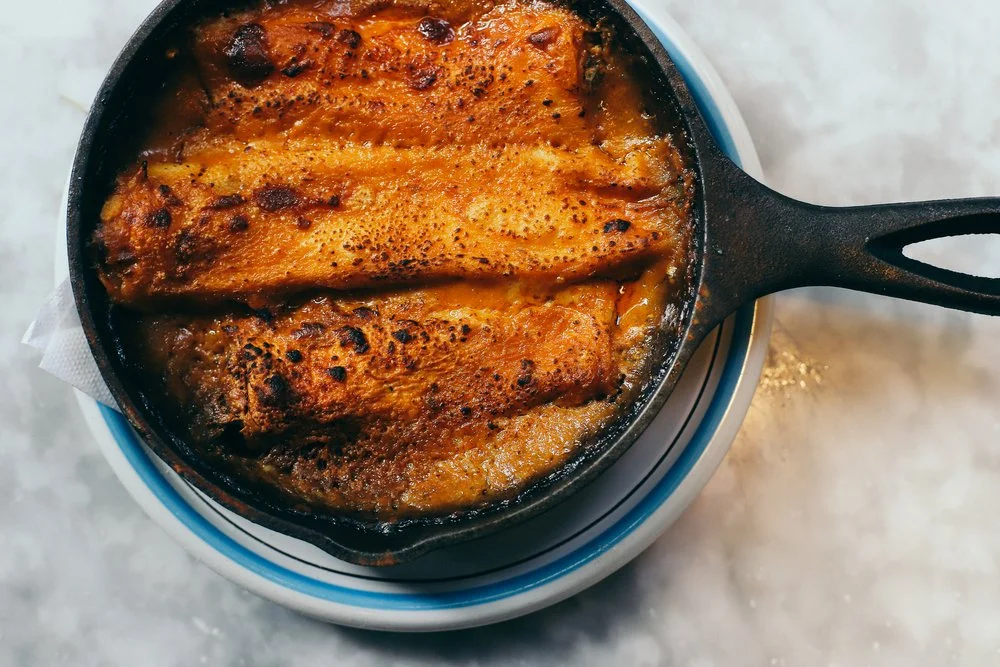 Baked cannelloni in tomato sauce in a cast iron skillet on a blue-rimmed plate