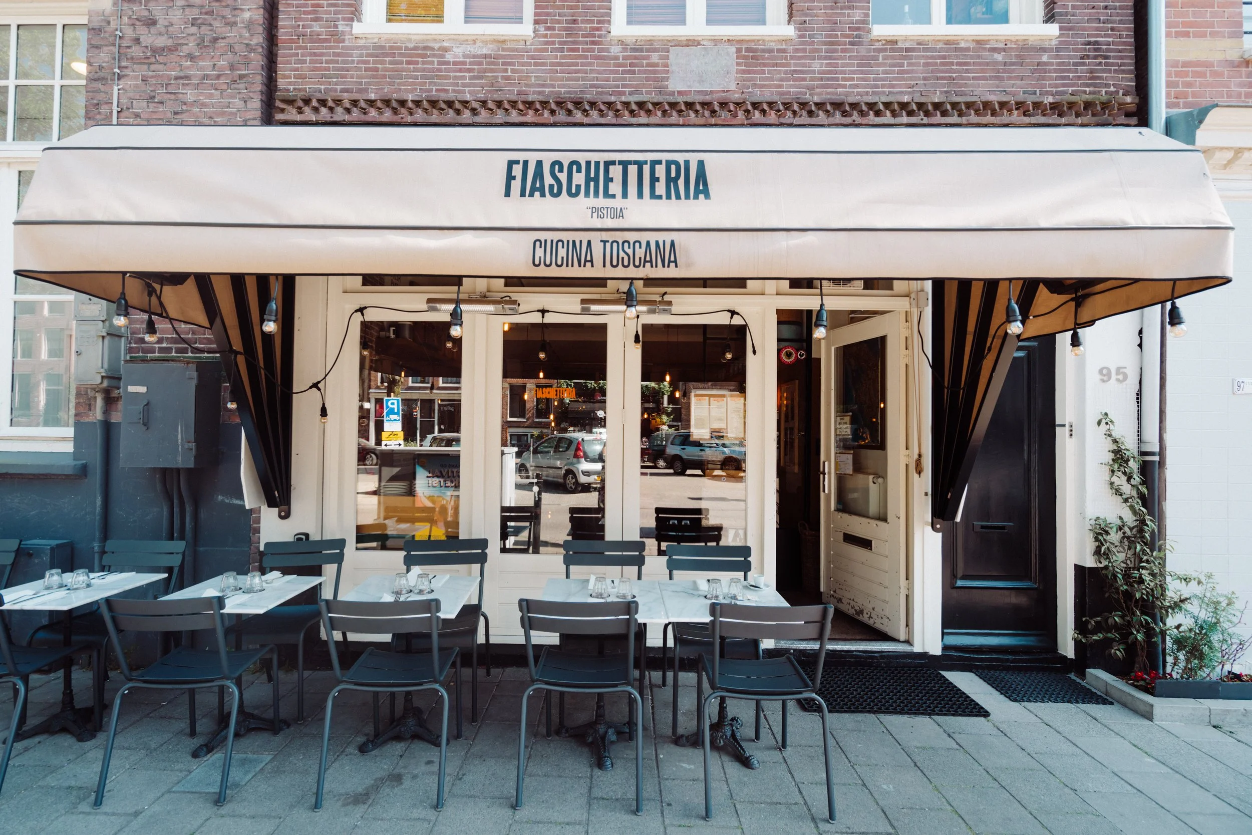 Cream awning of the Jordaan room with terrace tables and chairs on the sidewalk