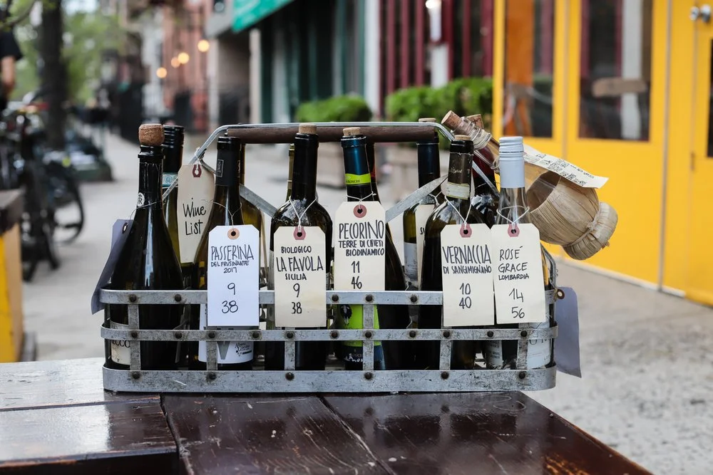 Metal wine crate of Italian bottles with handwritten price tags on an outdoor table