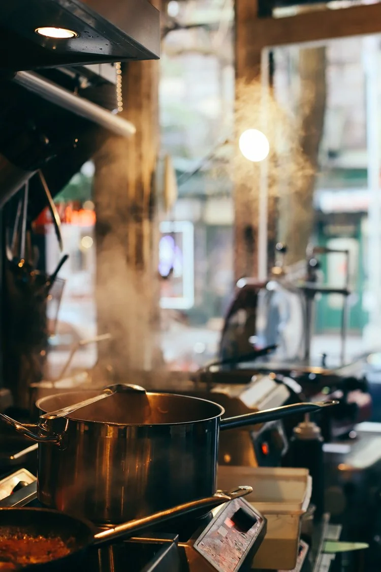 Restaurant kitchen with a steaming pot on the stove seen from the dining room
