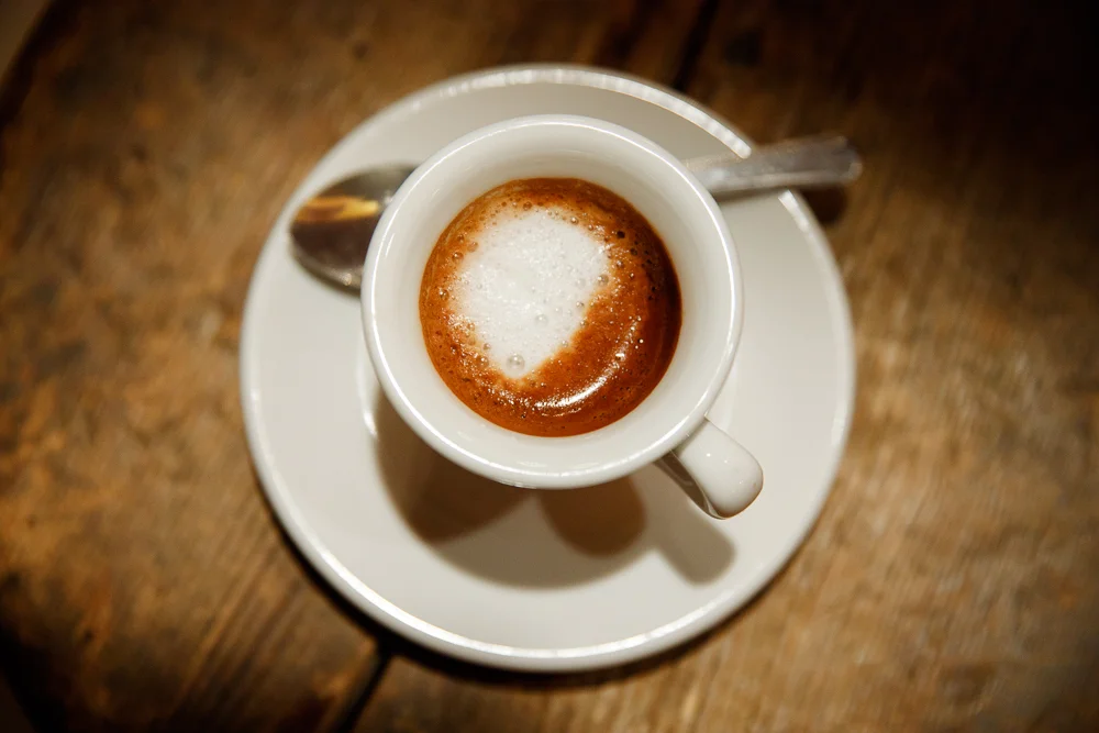 Single espresso cup on a saucer with a spoon on a wooden table