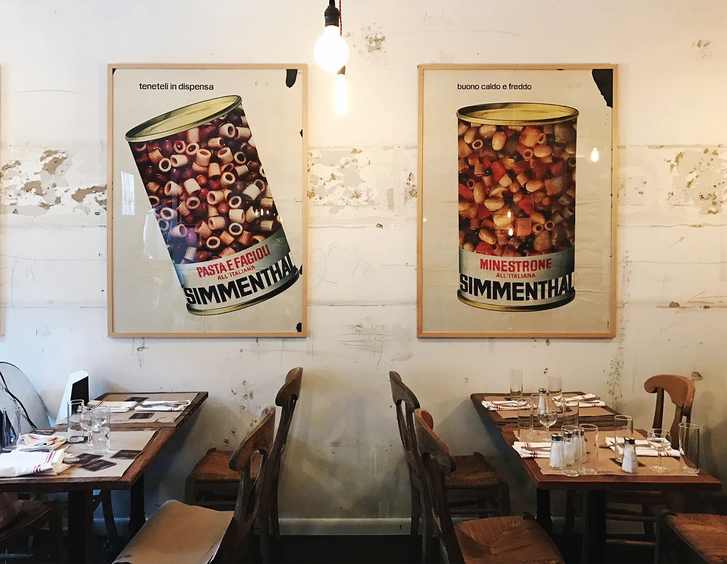 Dining room with two large framed vintage Simmenthal posters on a distressed white wall