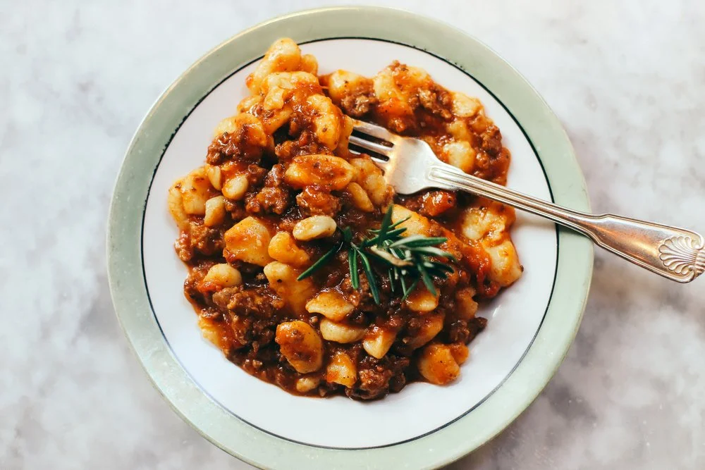 Gnocchi with meat ragù and rosemary in a green-rimmed bowl with a silver fork
