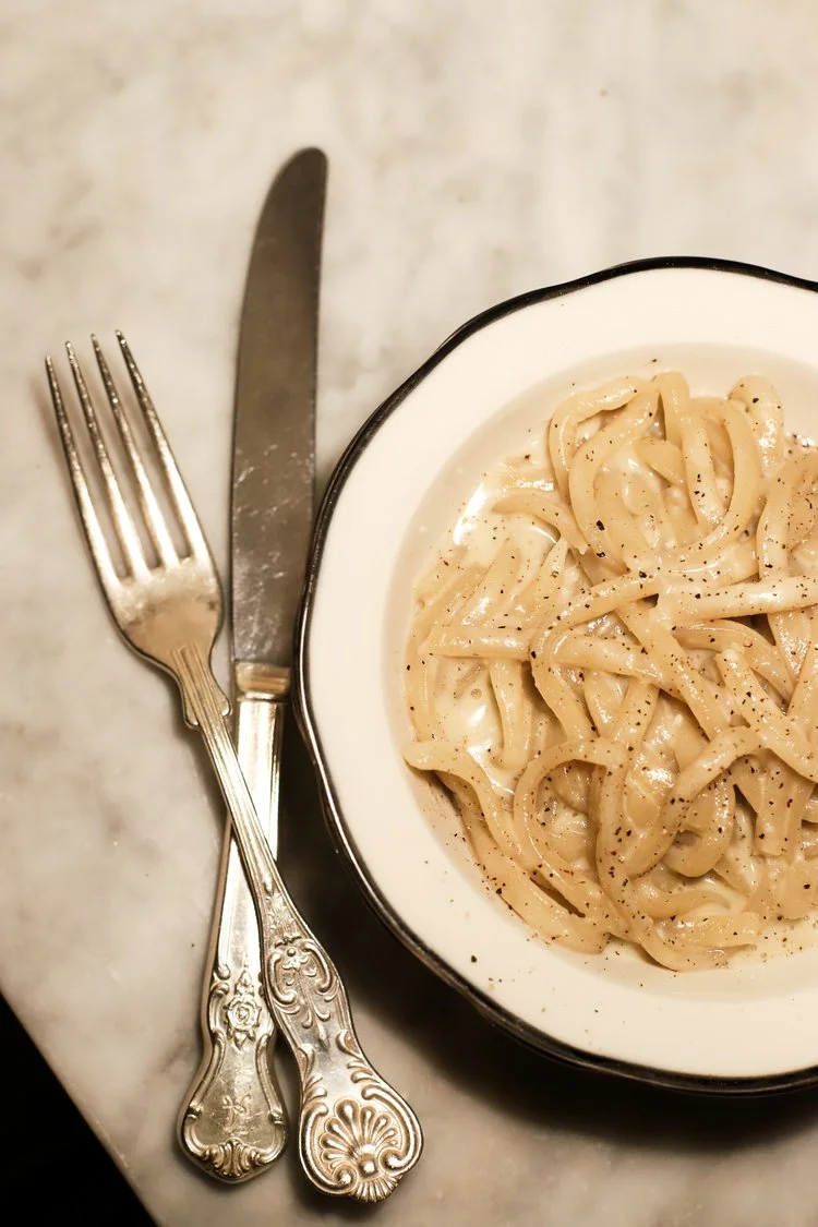 Bowl of tagliatelle in creamy cacio e pepe style sauce with silver cutlery on marble