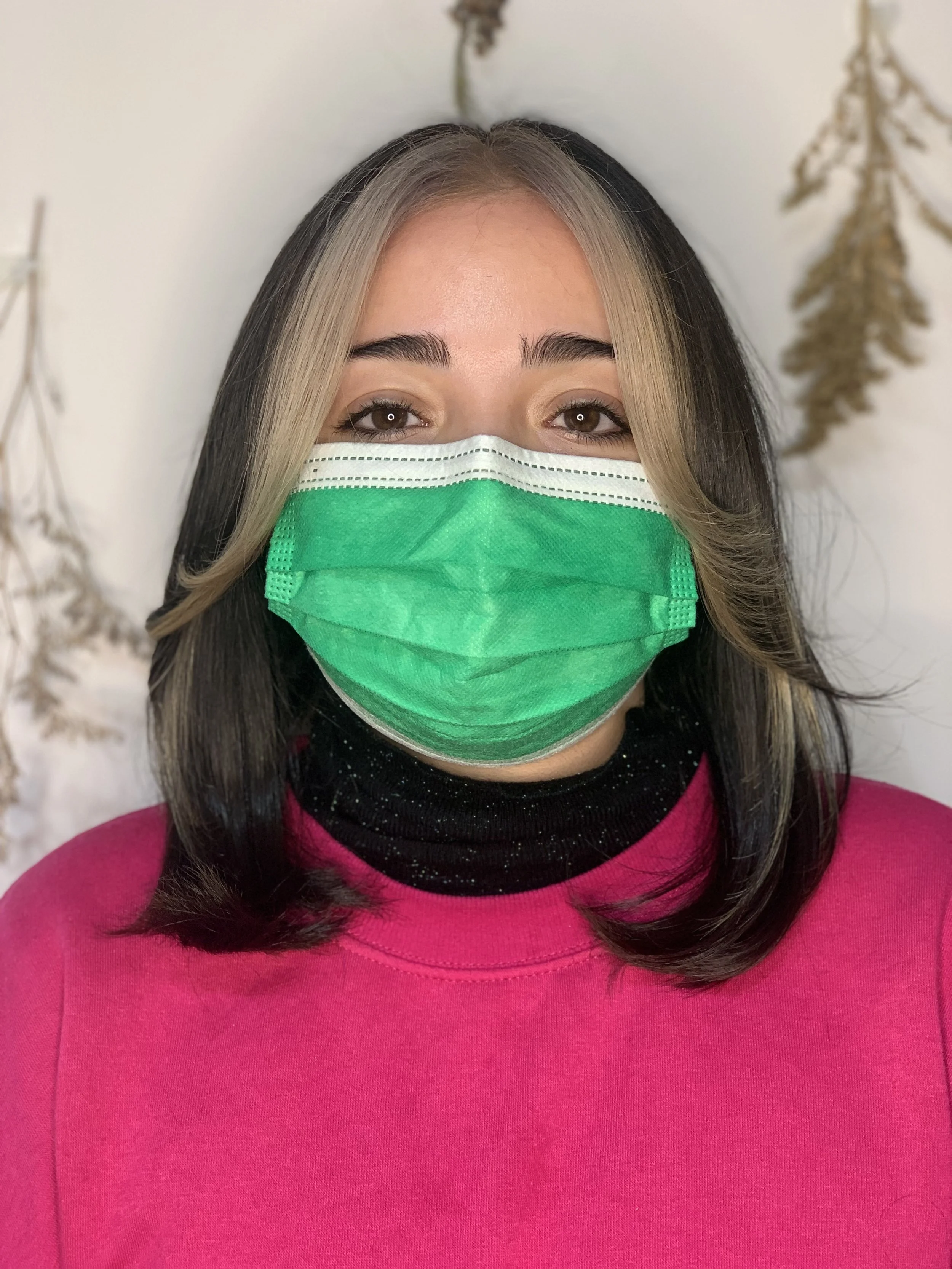 Client with dark hair and bright blonde money-piece highlights, wearing a green face mask and hot pink top