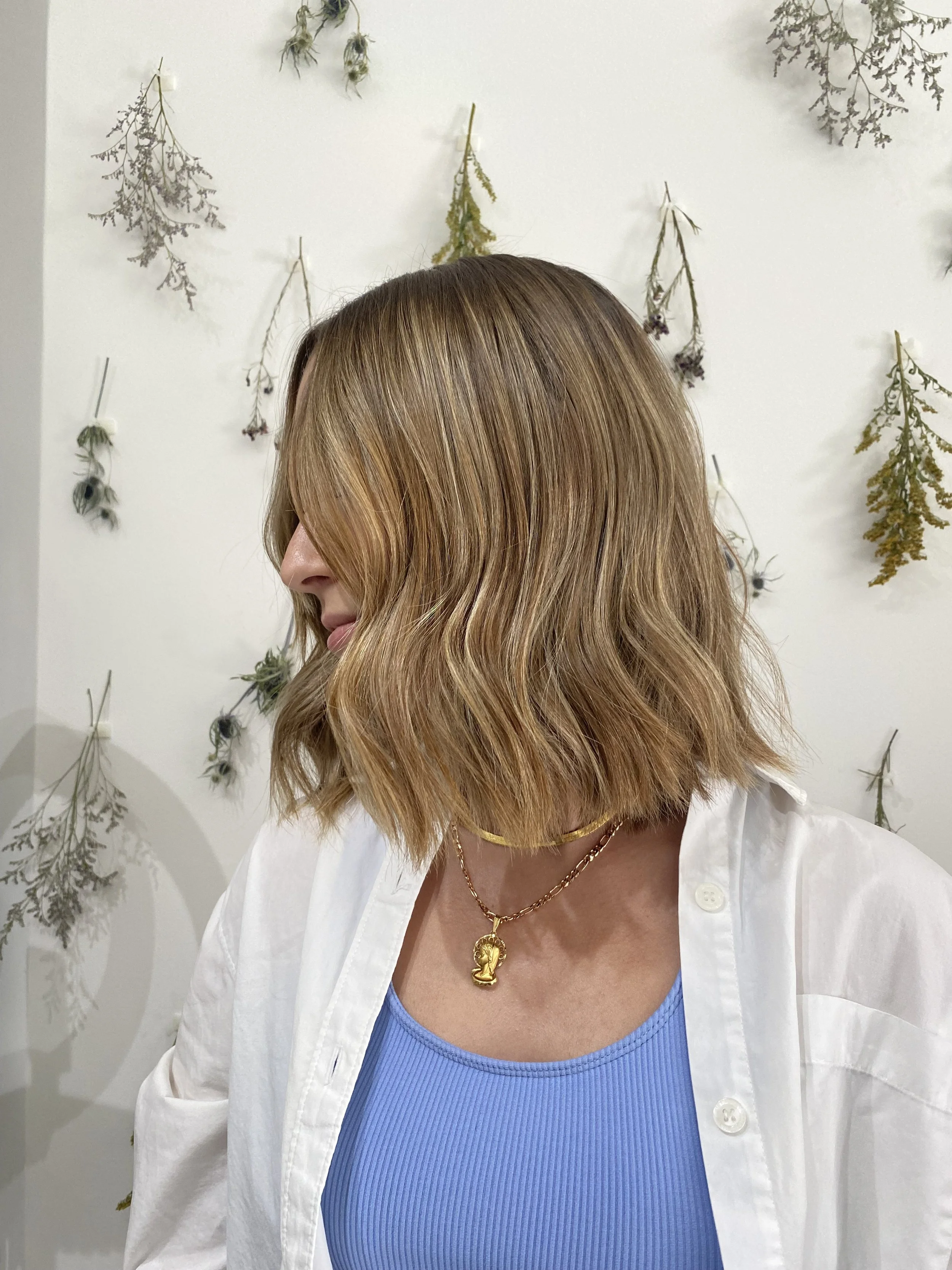 Wavy honey-blonde bob shown in side profile against a dried botanical backdrop at Green Velvet Parlor