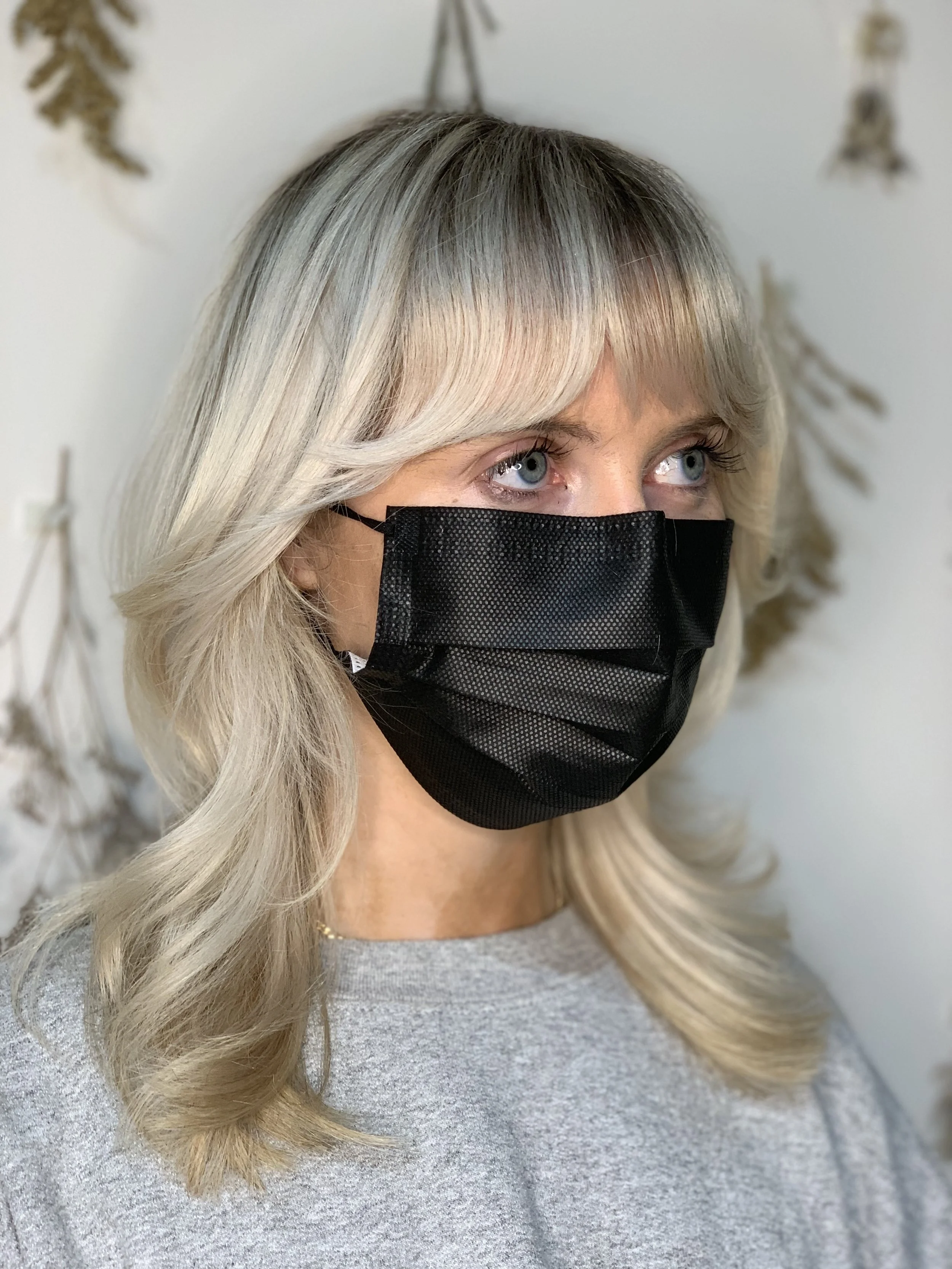 Platinum blonde layered haircut with bangs, client wearing a black face mask, styled at Green Velvet Parlor