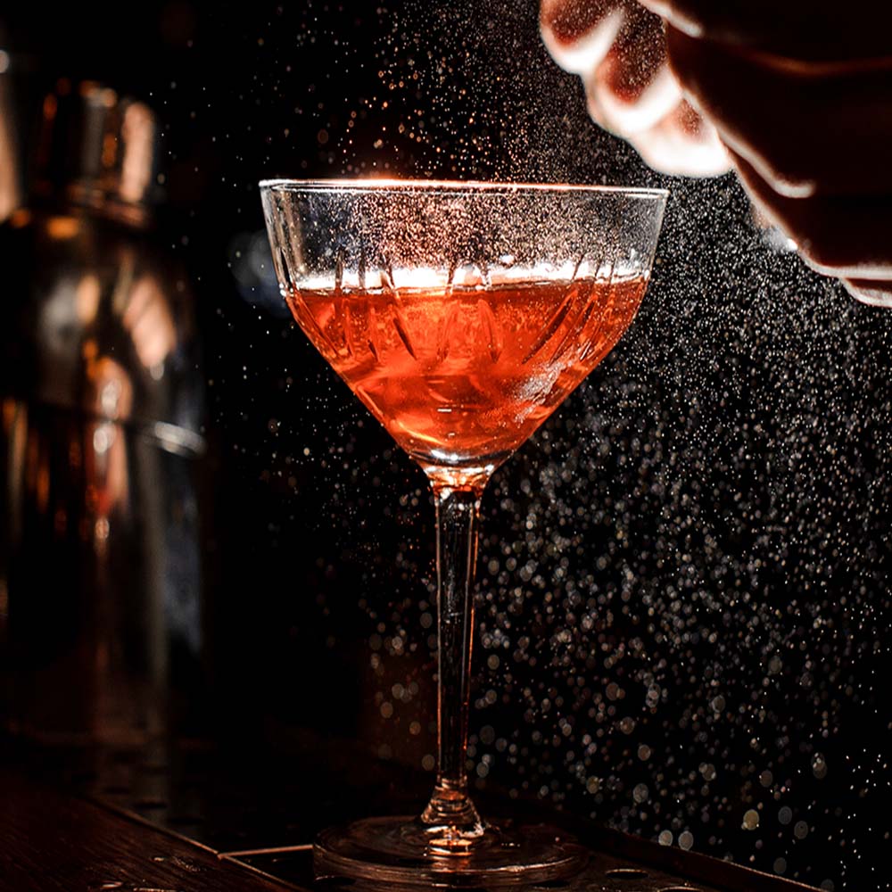 Cocktail in a coupe glass being spritzed at the dark bar