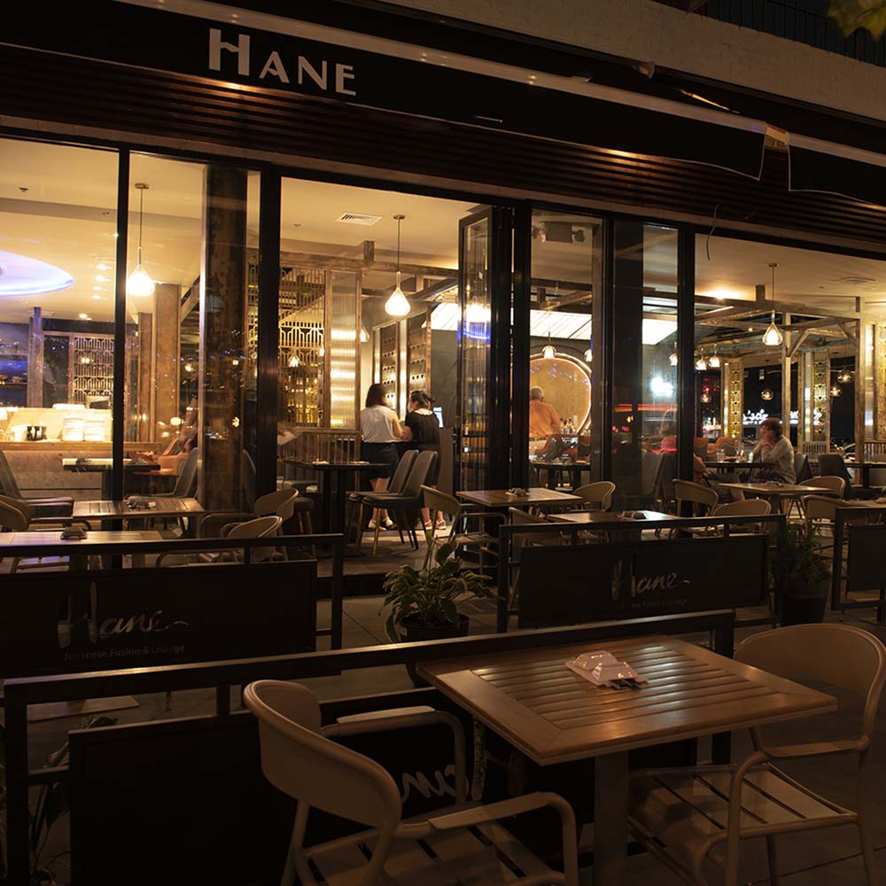 Hane exterior storefront at night with illuminated signage and patio tables