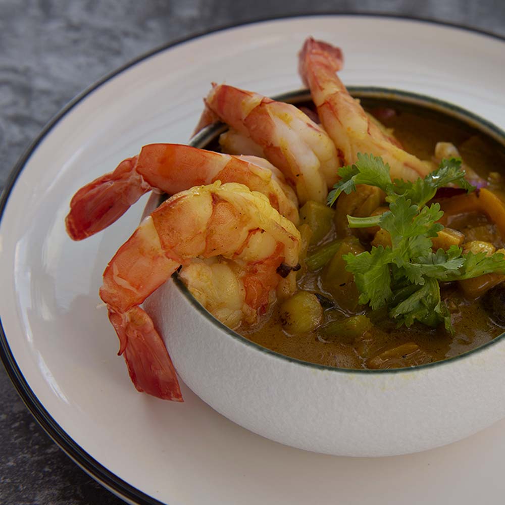 Shrimp curry in a white bowl garnished with whole shrimp and cilantro