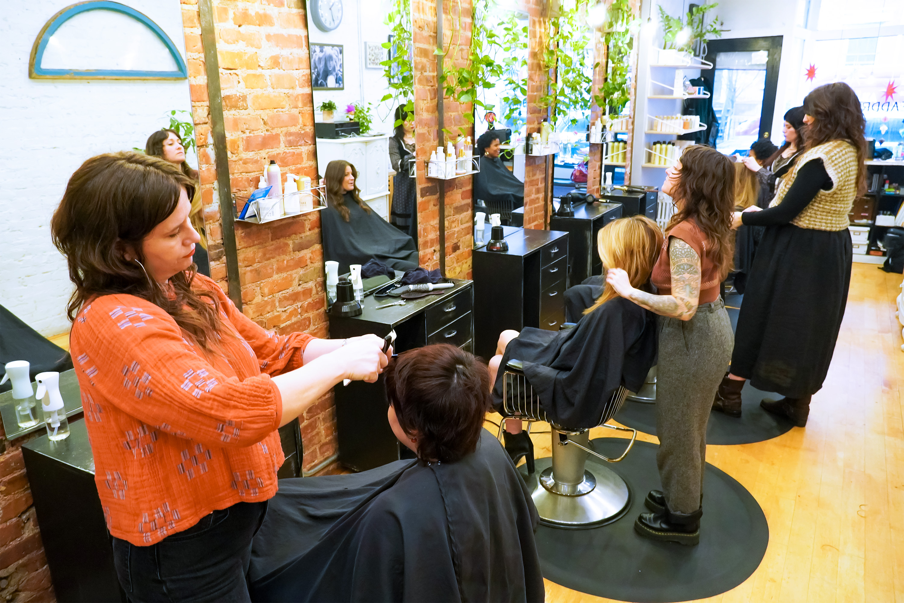 Multiple stylists working on clients at Headdress with brick walls, mirrors and plants