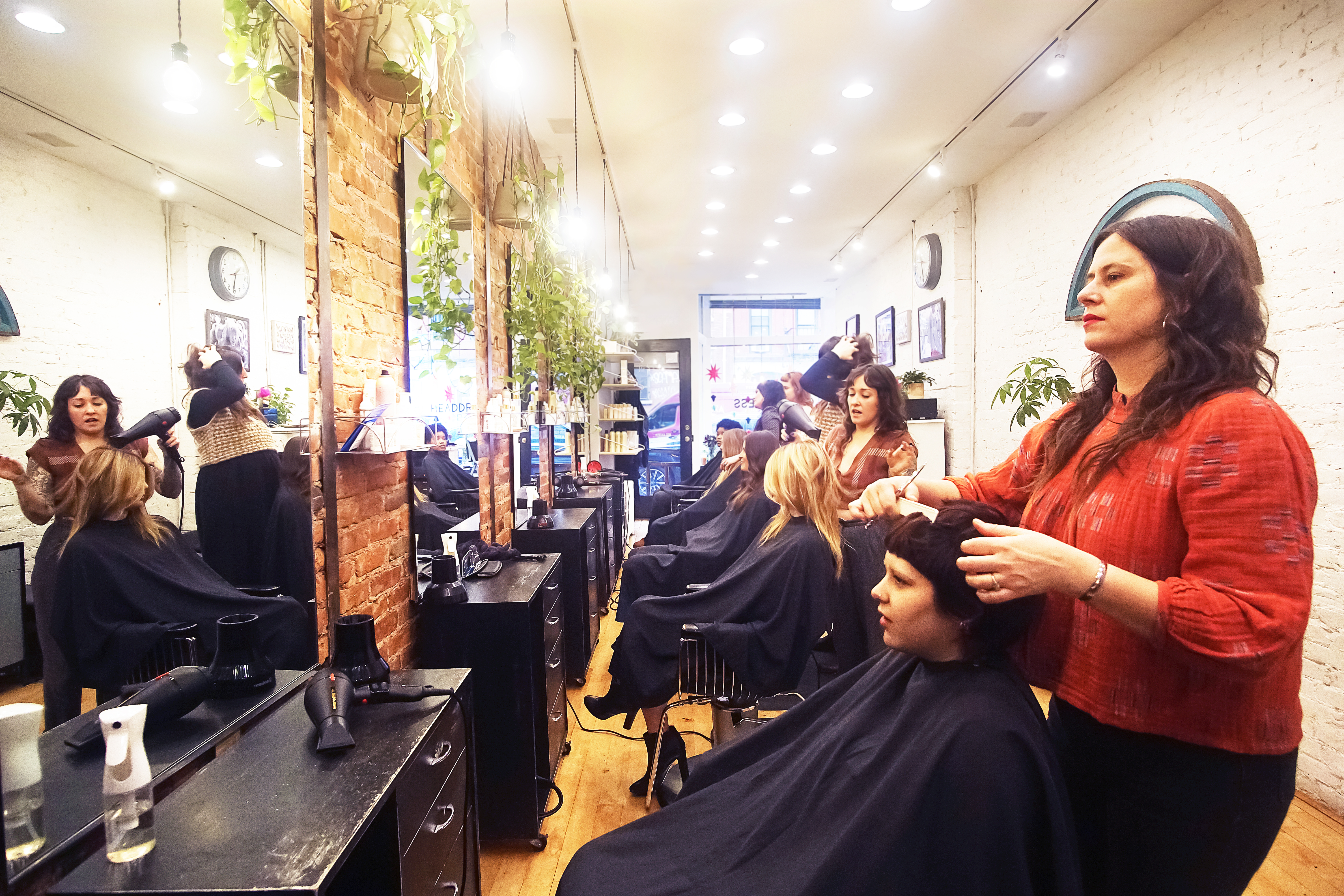 Stylists cutting and blow-drying clients' hair inside Headdress, brick walls and plants