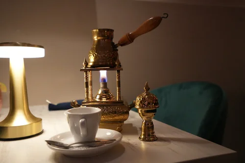 Brass Turkish coffee pot brewing over a flame with an espresso cup