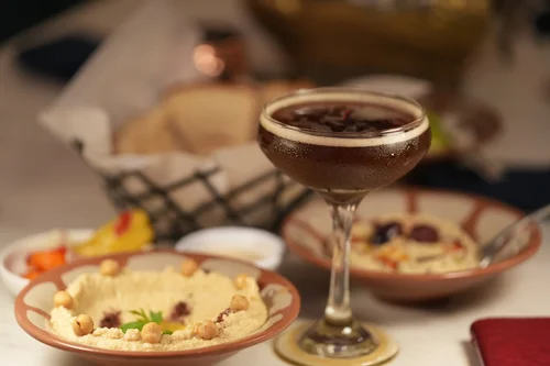Espresso martini alongside bowls of hummus and a bread basket