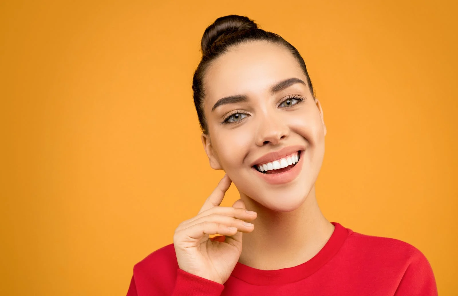 Smiling young woman with her hand at her cheek against a warm amber background