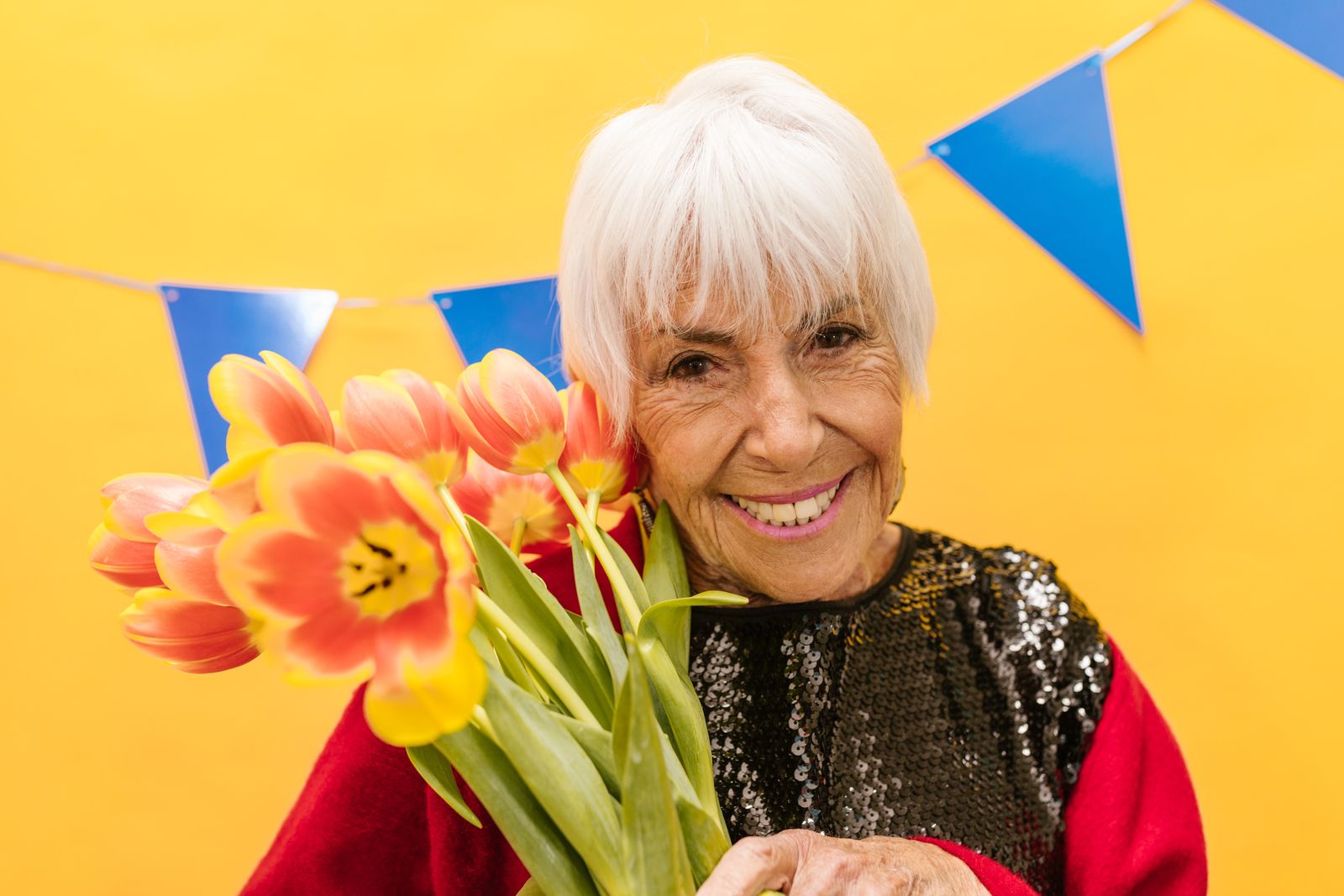 An older woman with white hair smiling and holding pink and yellow tulips