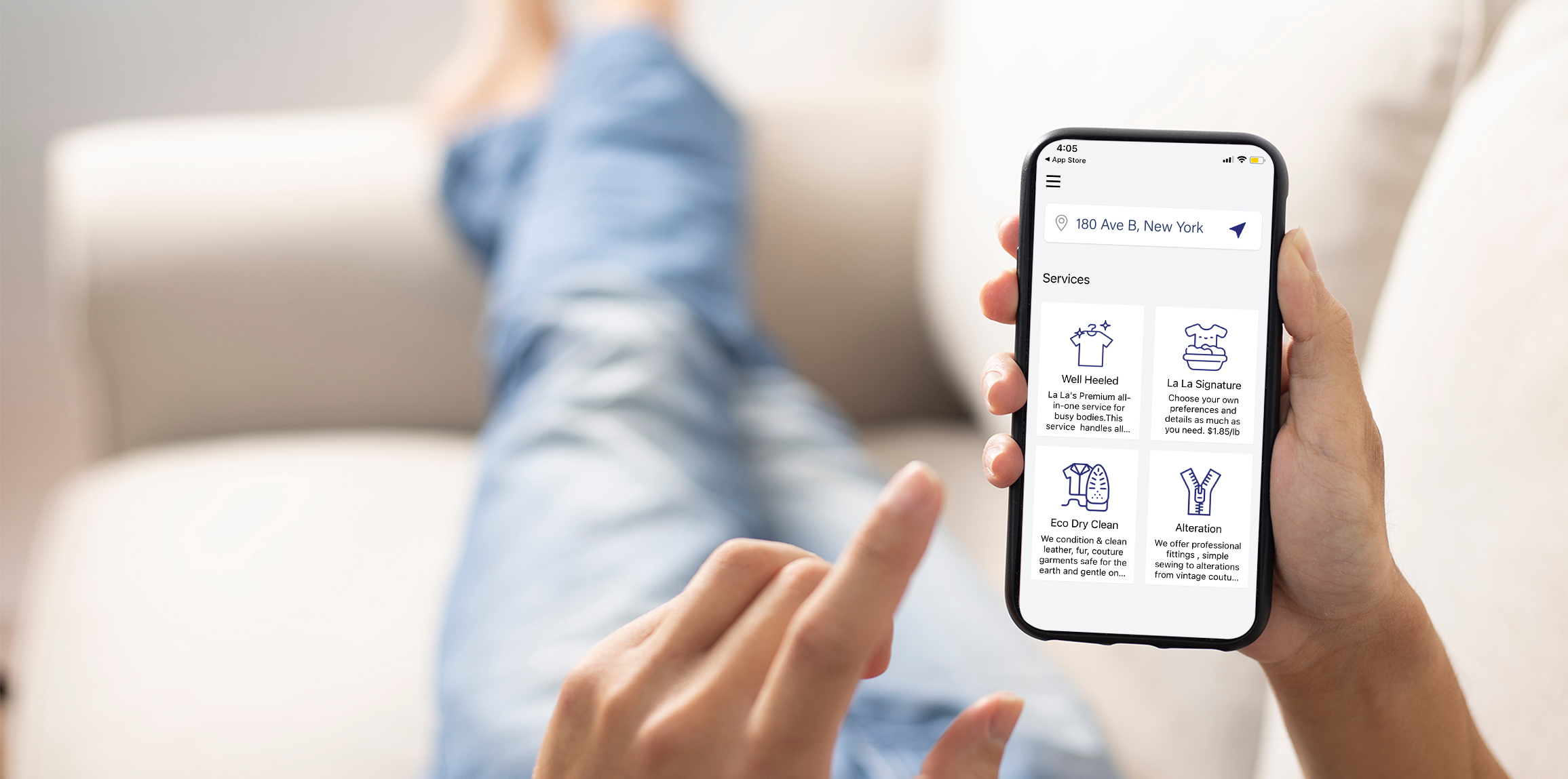 Person relaxing on a sofa holding a smartphone showing the La La Laundry app