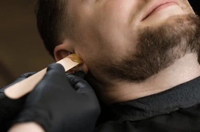 Wax applied near a client's ear with a spatula