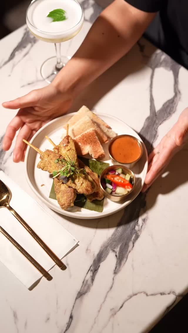 Overhead view of chicken satay skewers with roti, peanut sauce and pickled vegetables on a marble table